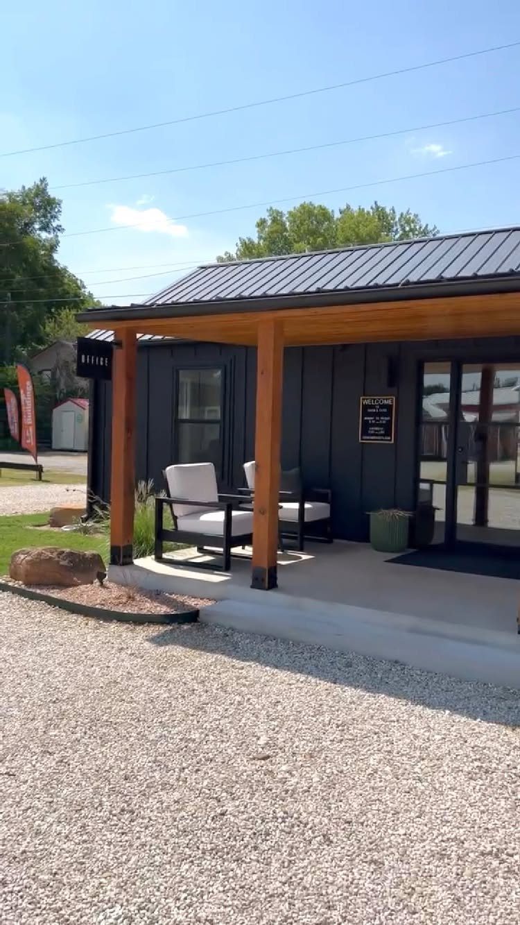 A modern dark grey backyard studio with a wooden porch and white outdoor chairs.