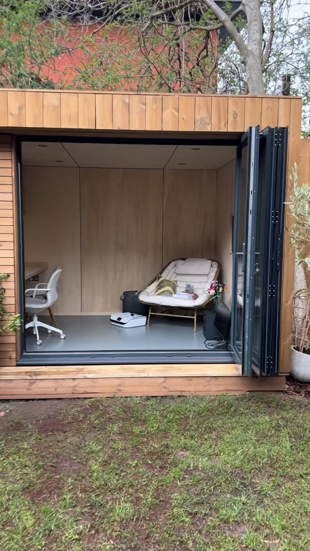 A modern wooden garden studio with open bi-fold doors revealing a minimalist interior workspace.