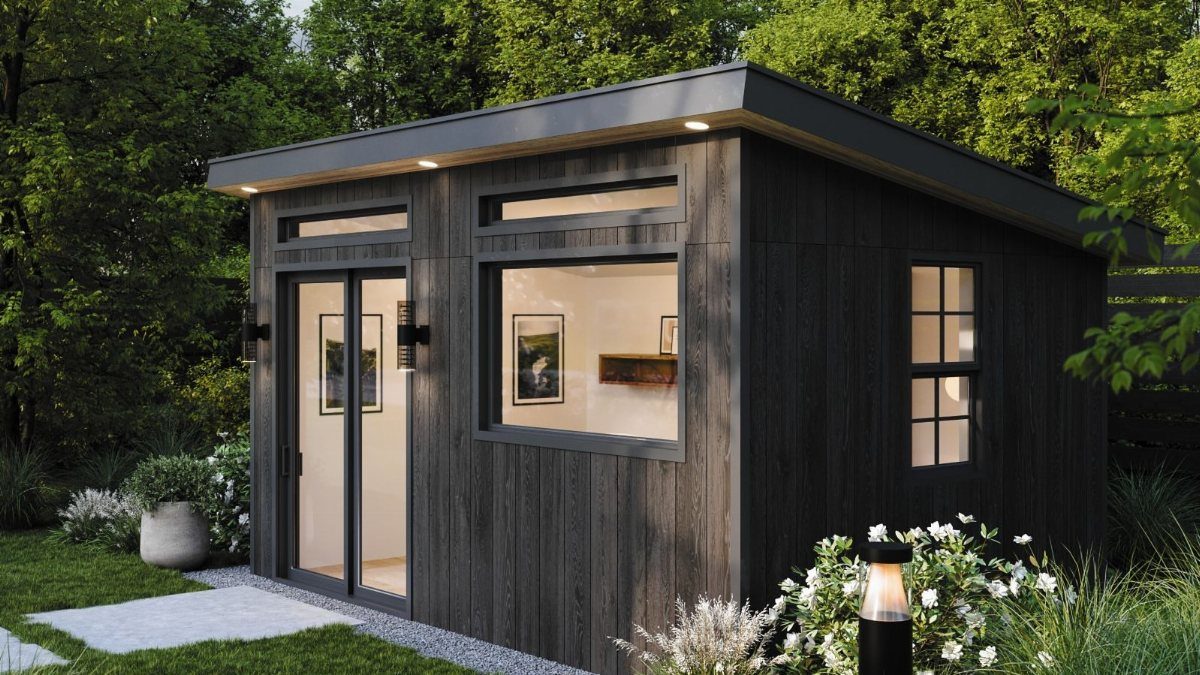 Modern dark wood backyard studio shed with large glass windows and doors in a garden.