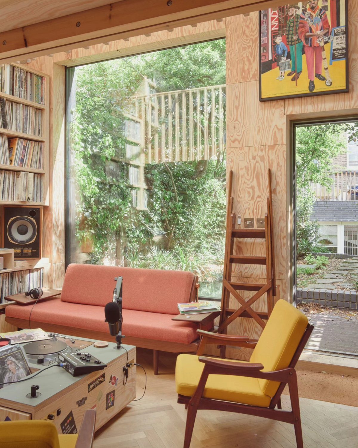 Music production equipment and vinyl records inside a bright, wood-paneled studio with large windows.