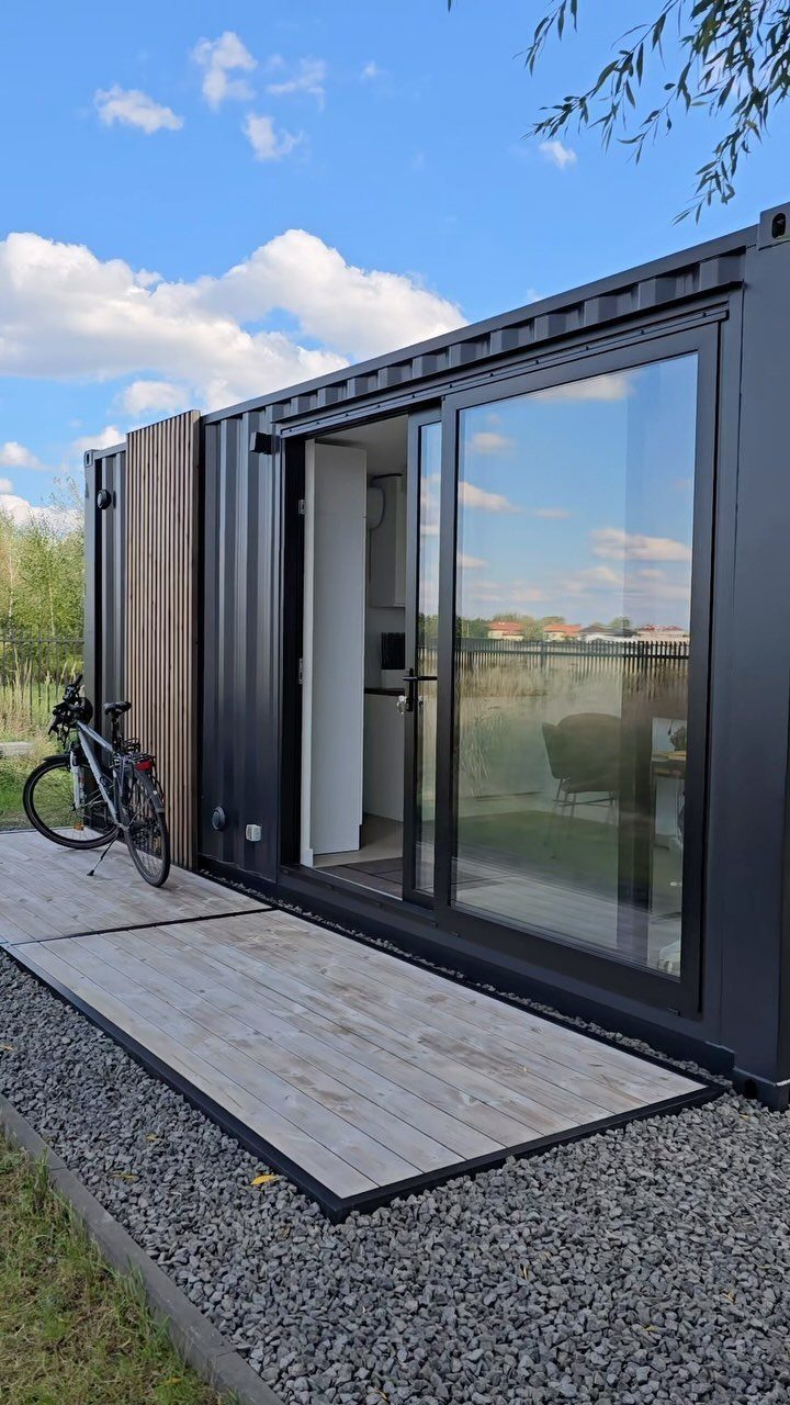 A black shipping container converted into a modern backyard studio with glass doors and a wooden deck.