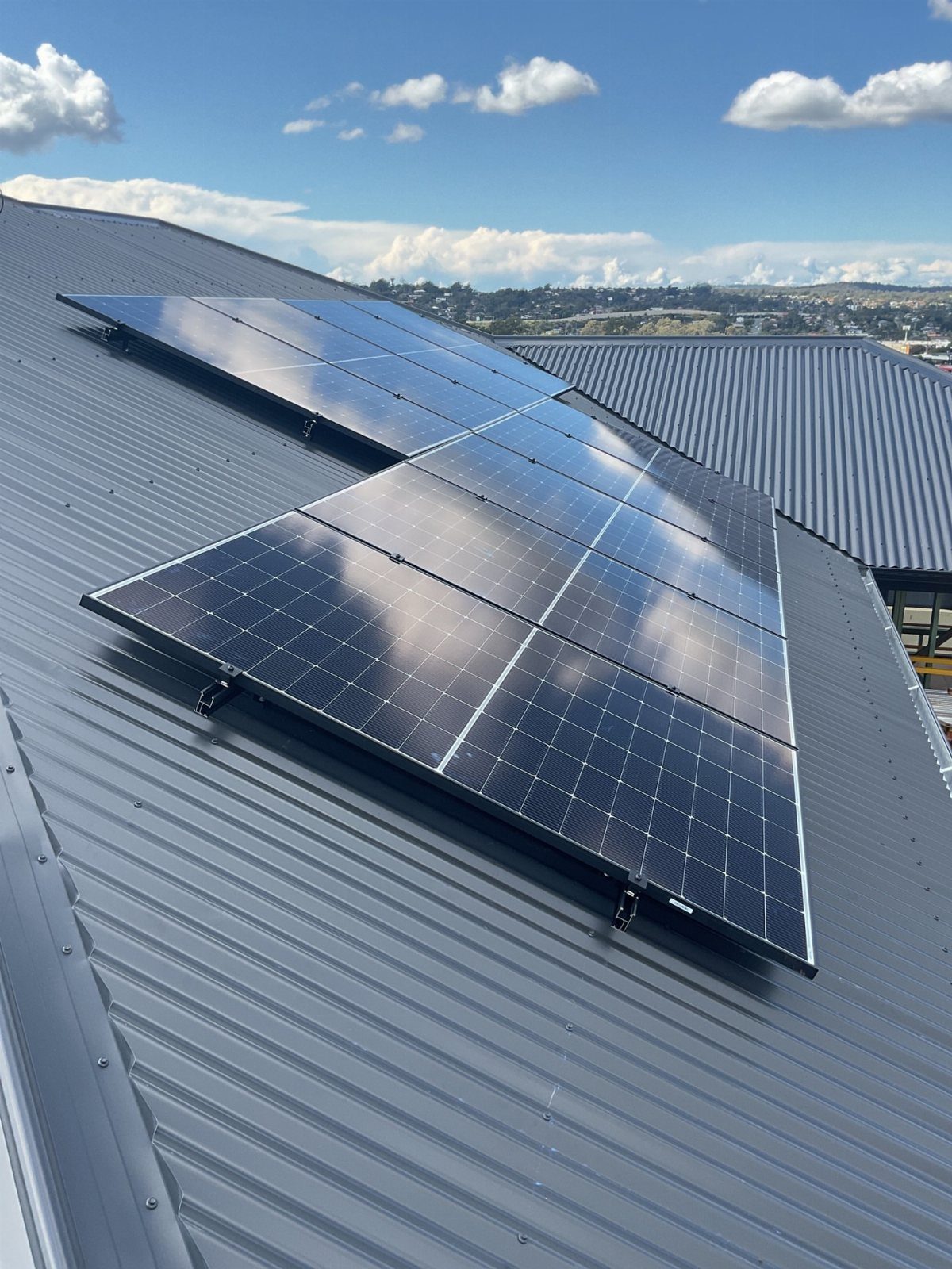 Solar panels mounted on a grey corrugated metal roof against a blue sky.