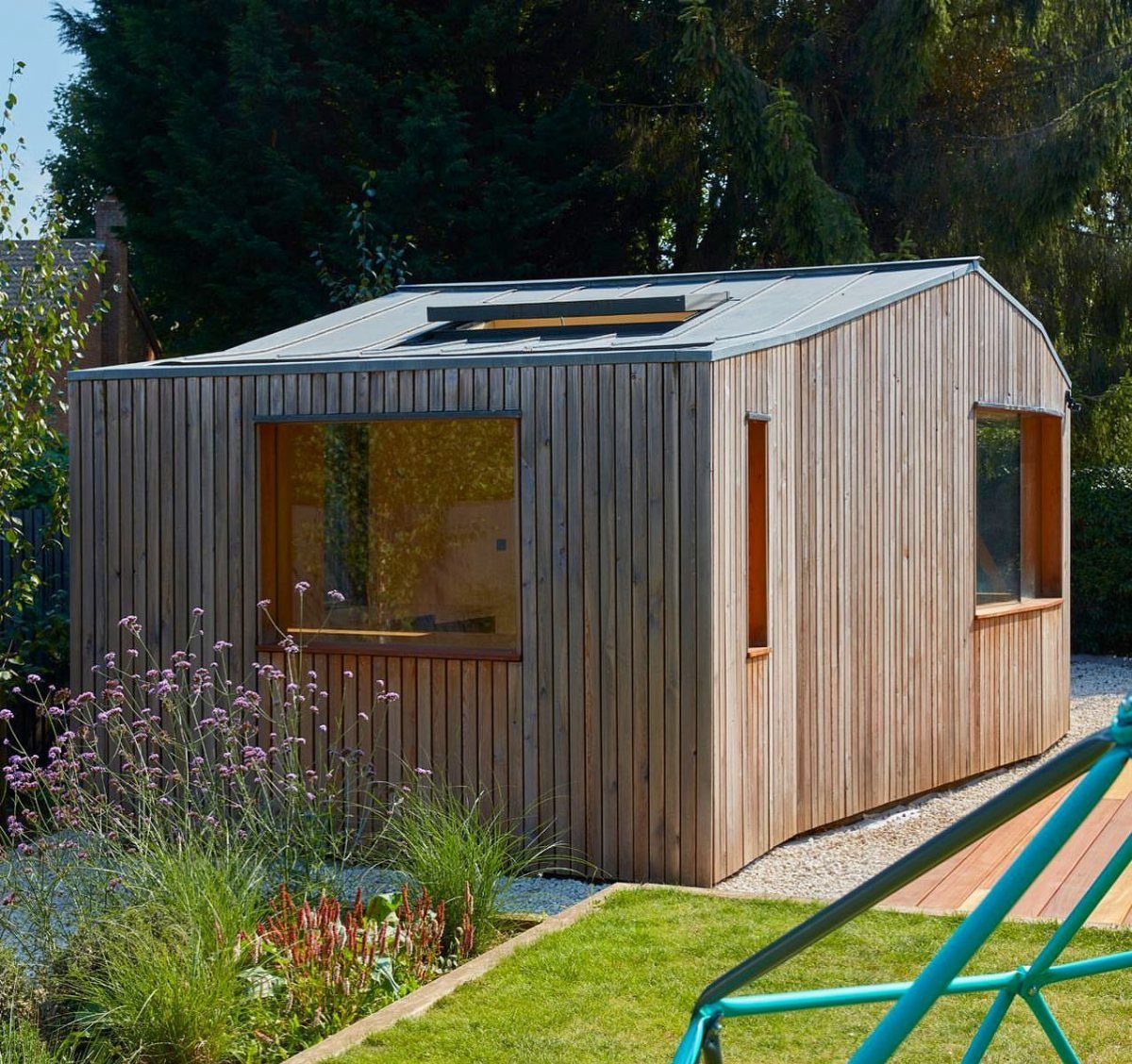 A modern wooden garden studio with vertical timber cladding and large windows in a backyard.