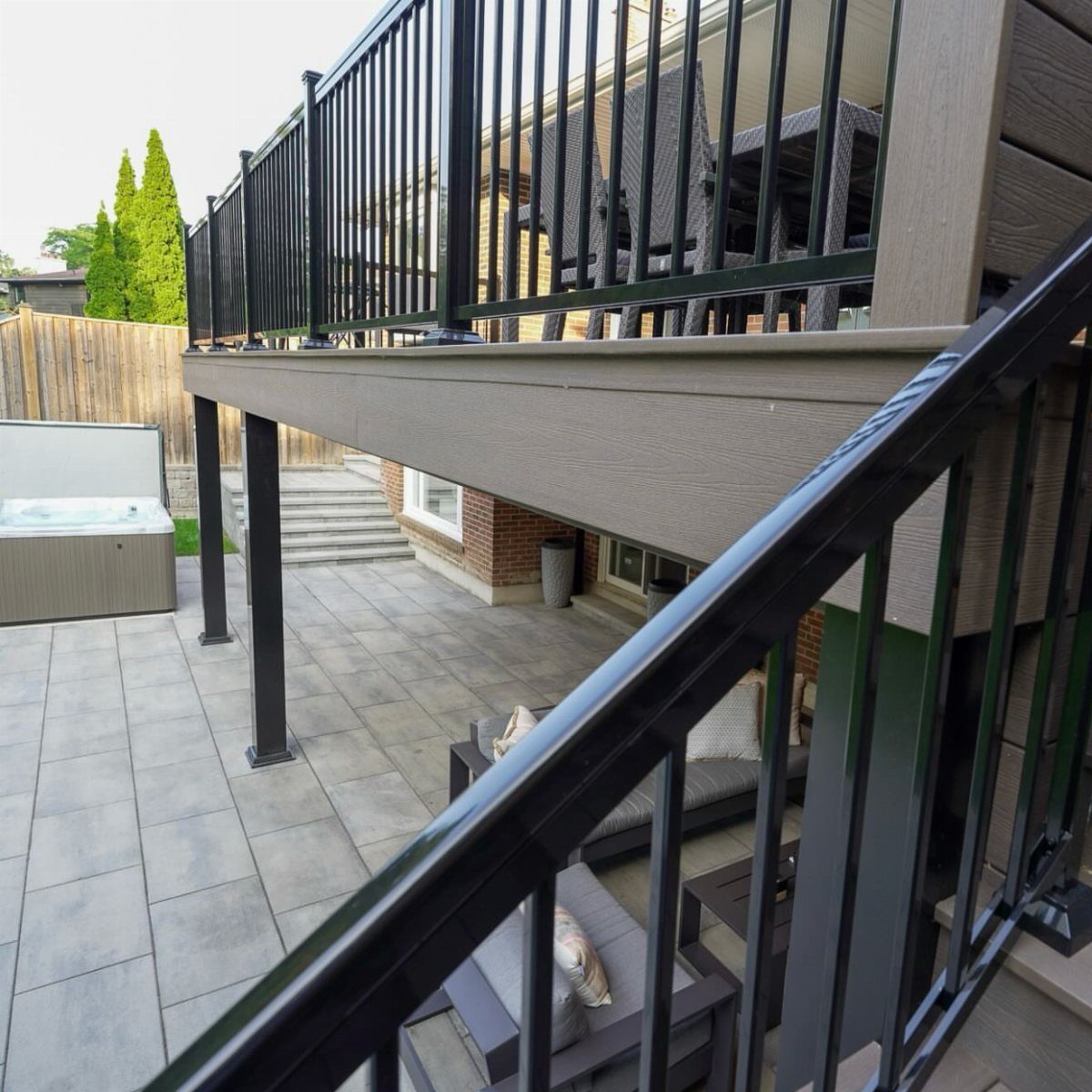 3 Room Under Deck Ideas for Leftover Space 3 A paved patio area with lounge furniture located underneath a raised wooden deck.