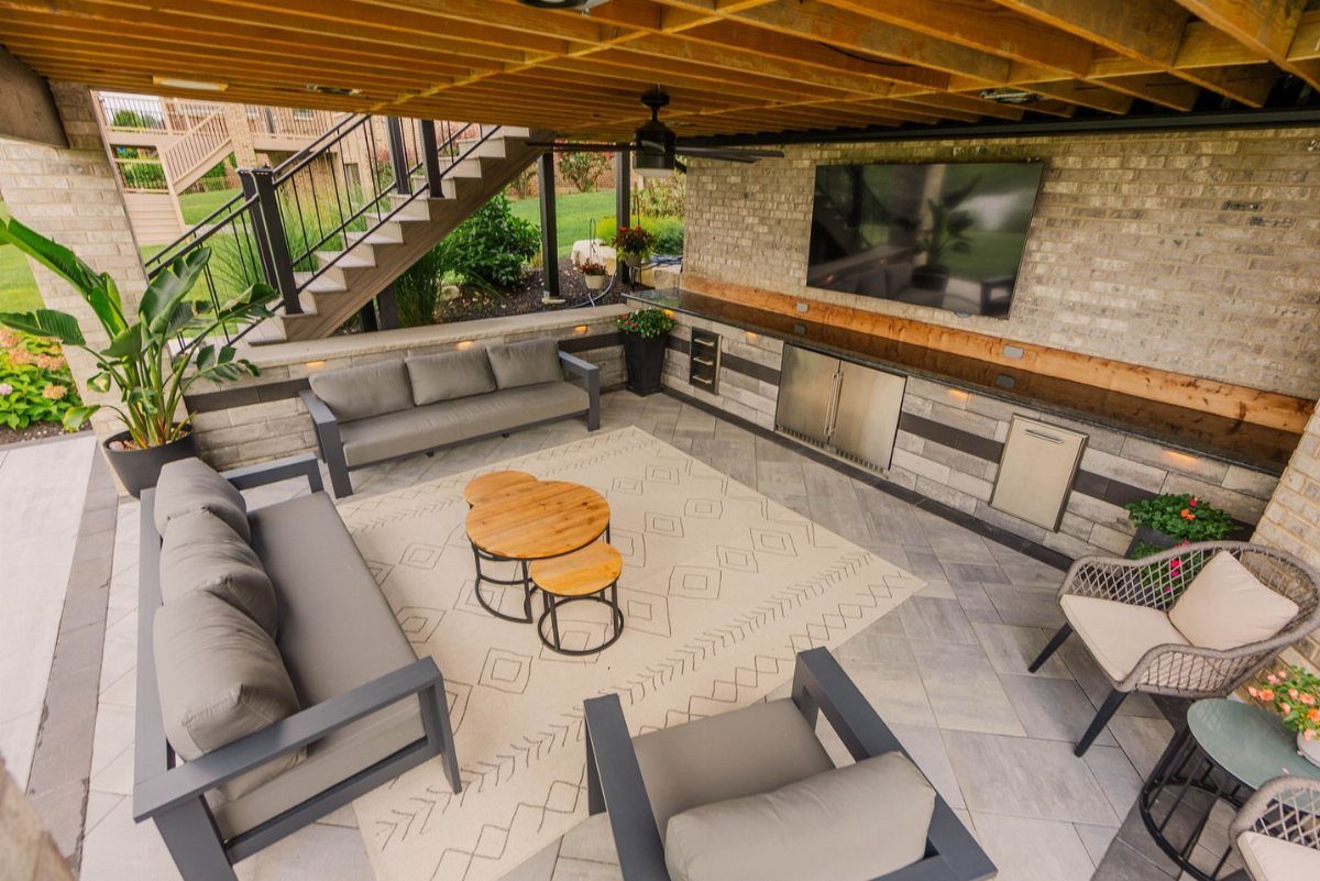 3 Room Under Deck Ideas for Leftover Space 2 Grey outdoor furniture arranged on a patterned rug under a wooden deck structure.