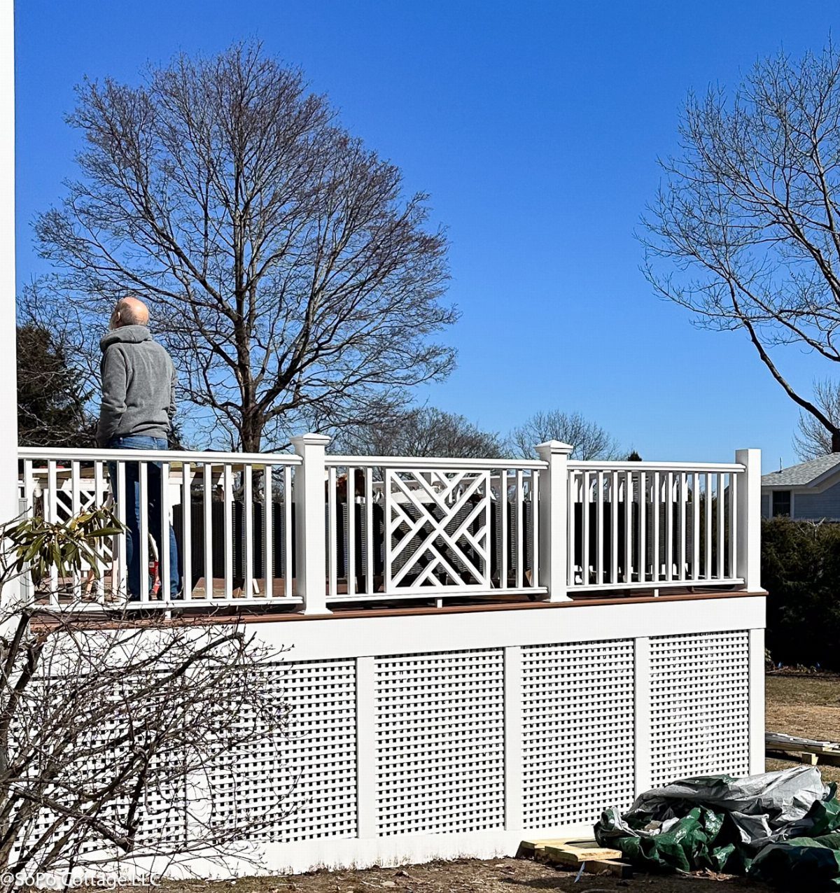 A white wooden side deck with decorative lattice railings and skirting under a blue sky.
