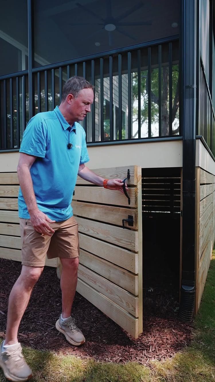 A man opening a built-in wooden storage compartment located under a raised deck.