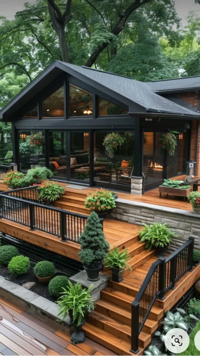 A multi-level wooden side deck with black railings and various green plants surrounding the stairs.