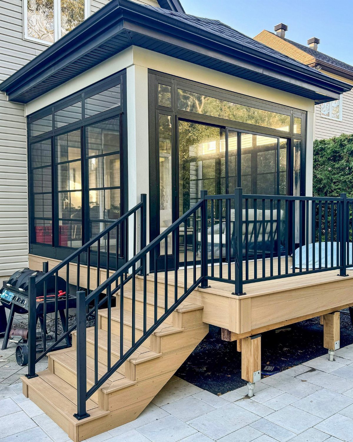 A light wood composite deck with black metal railings and stairs attached to a sunroom.