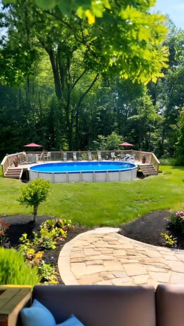 A blue above-ground pool surrounded by a wooden deck in a green backyard.