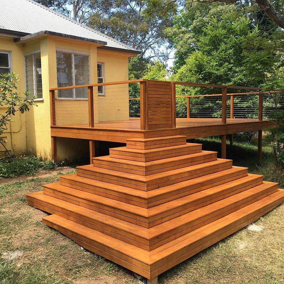Tiered wooden steps cascade down from an elevated backyard deck attached to a yellow house.