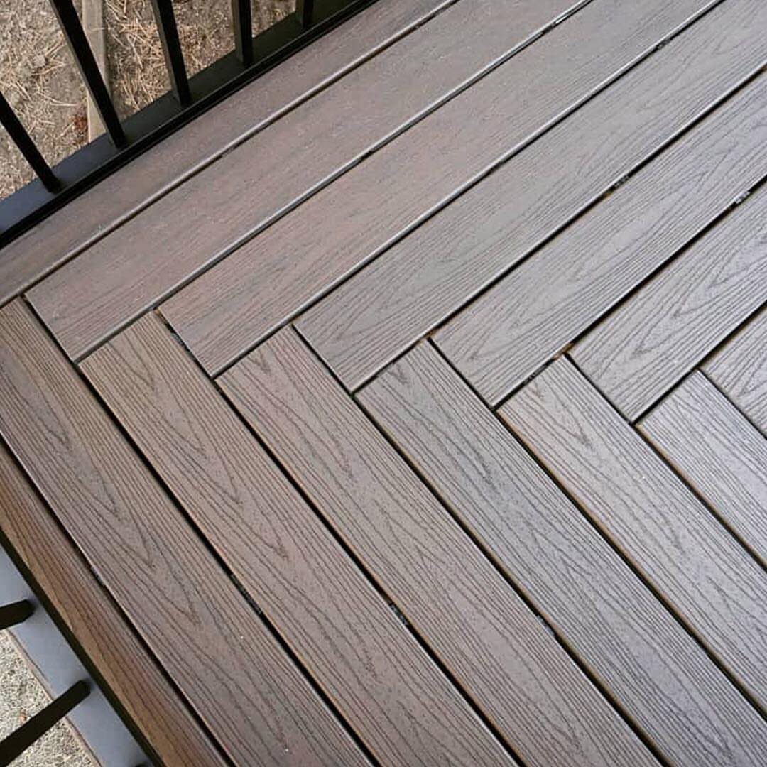 Dark brown composite deck boards arranged in a diagonal herringbone pattern with black metal railing.