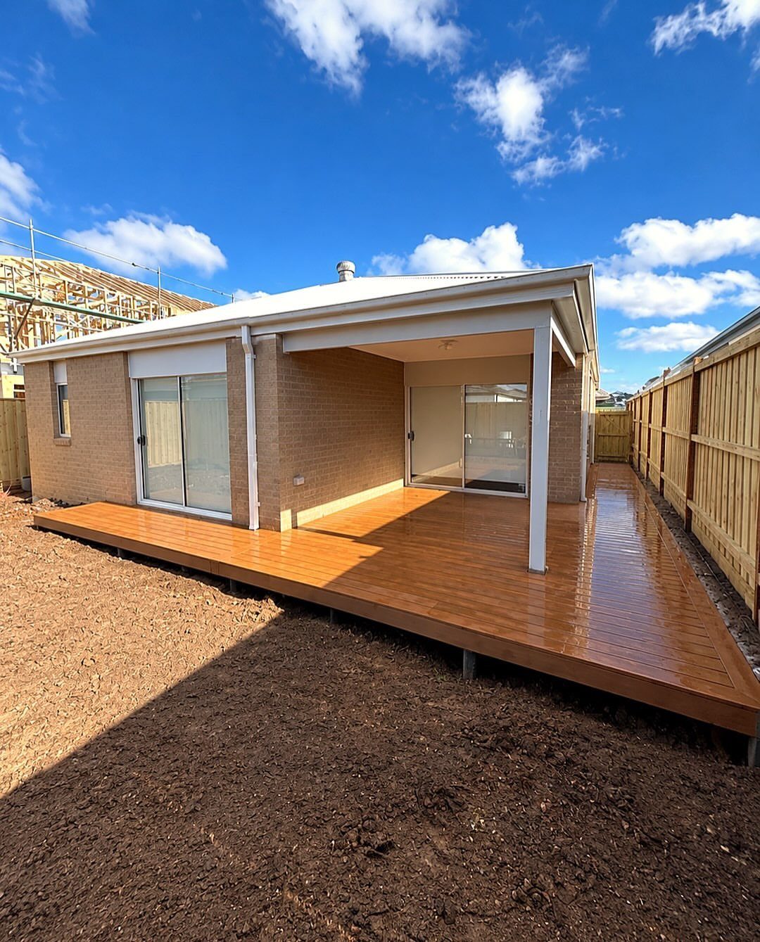 A low wooden deck wrapping around a brick house with sliding glass doors and a covered patio.