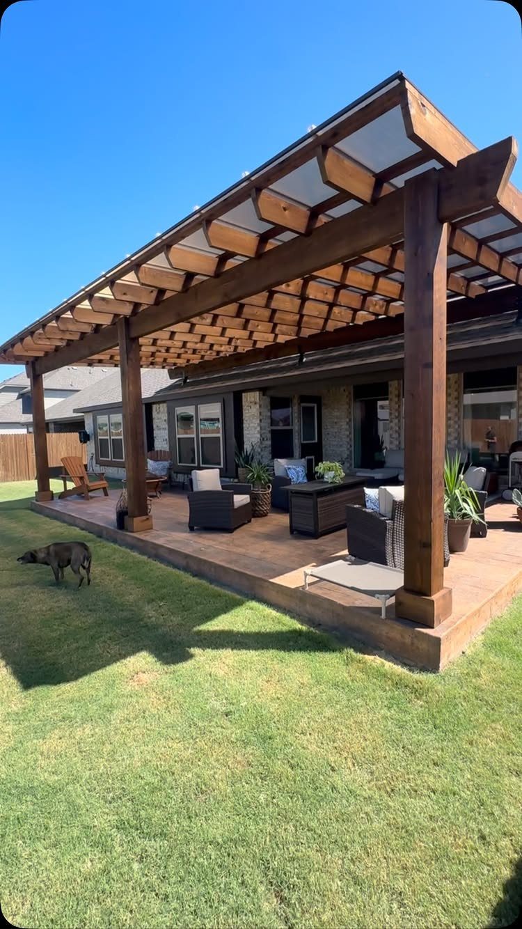 A wooden pergola with a translucent roof covering a furnished outdoor deck next to a lawn.