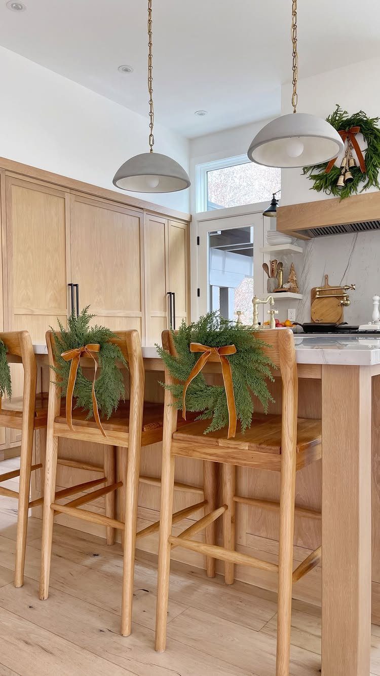 Wooden bar stools decorated with small evergreen wreaths and orange ribbons in a bright kitchen.