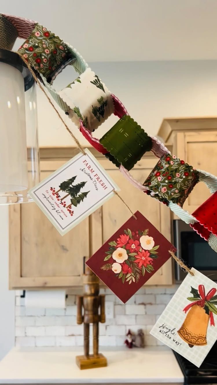 Holiday greeting cards hanging from a decorative fabric loop garland in a kitchen setting.