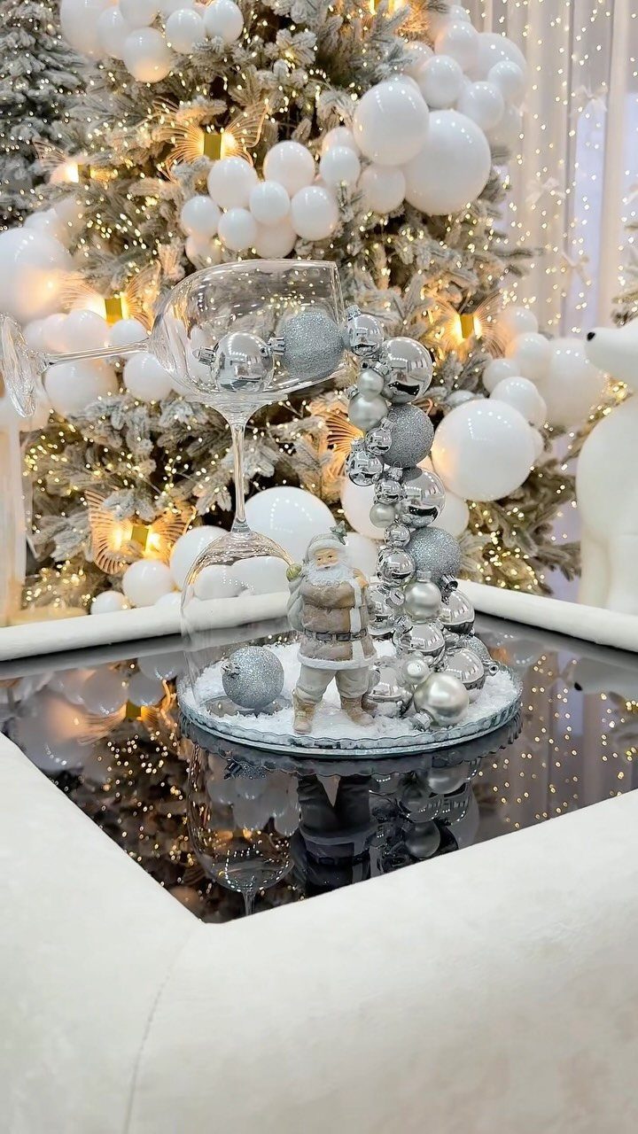 Silver ornaments and a Santa figurine inside a glass cloche on a coffee table.