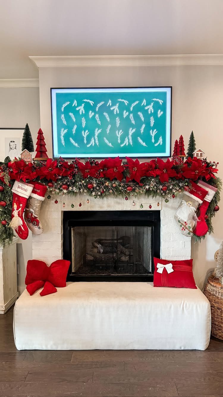 A decorated white fireplace mantel with red poinsettia garland and hanging Christmas stockings.