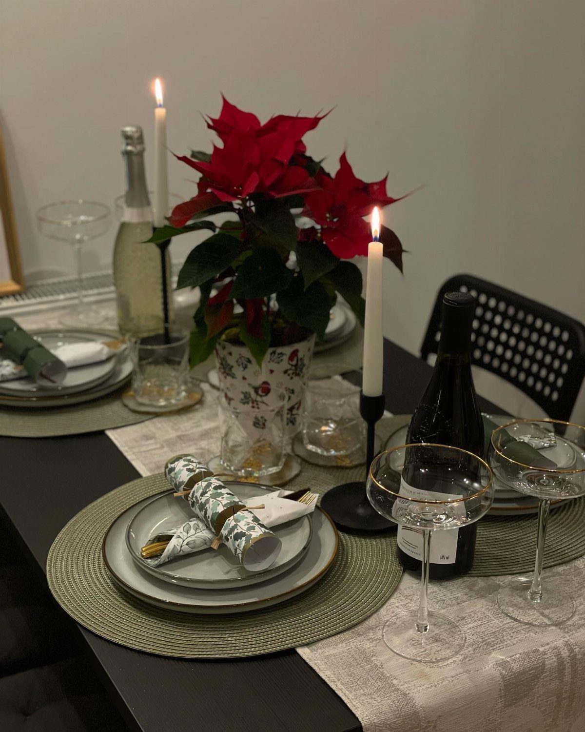 A festive holiday table setting with poinsettias, lit candles, and patterned Christmas crackers.