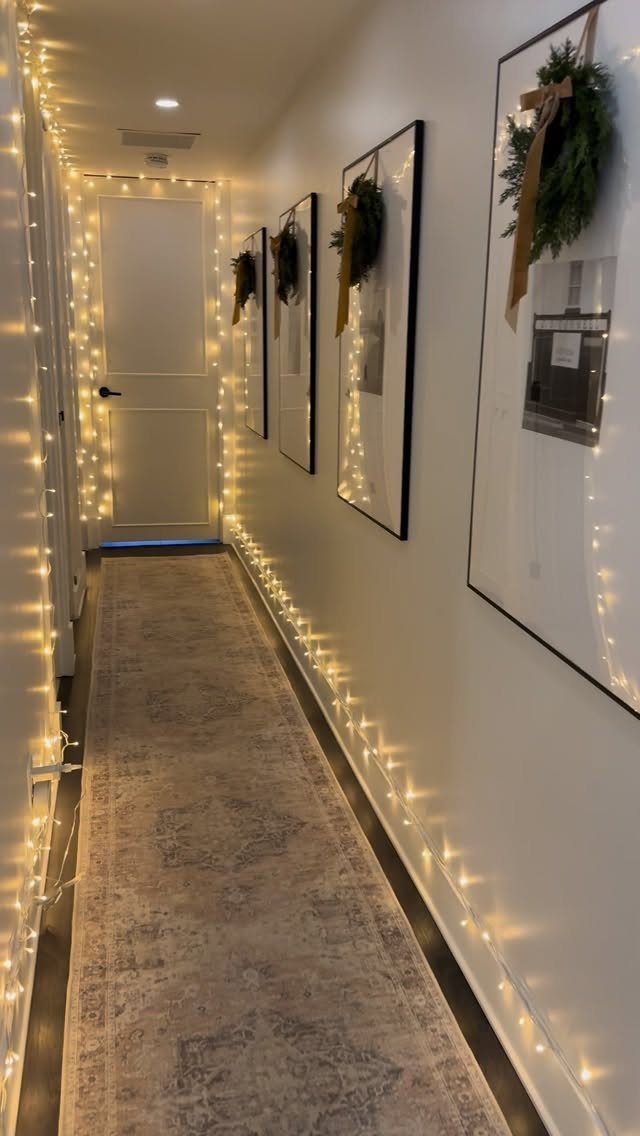 Warm white string lights line a narrow hallway decorated with small wreaths on framed wall art.